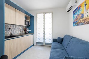 Cuina moderna amb armaris de fusta, microones i cafetera. Hi ha un sofà blau i un quadre d'un far a la paret.