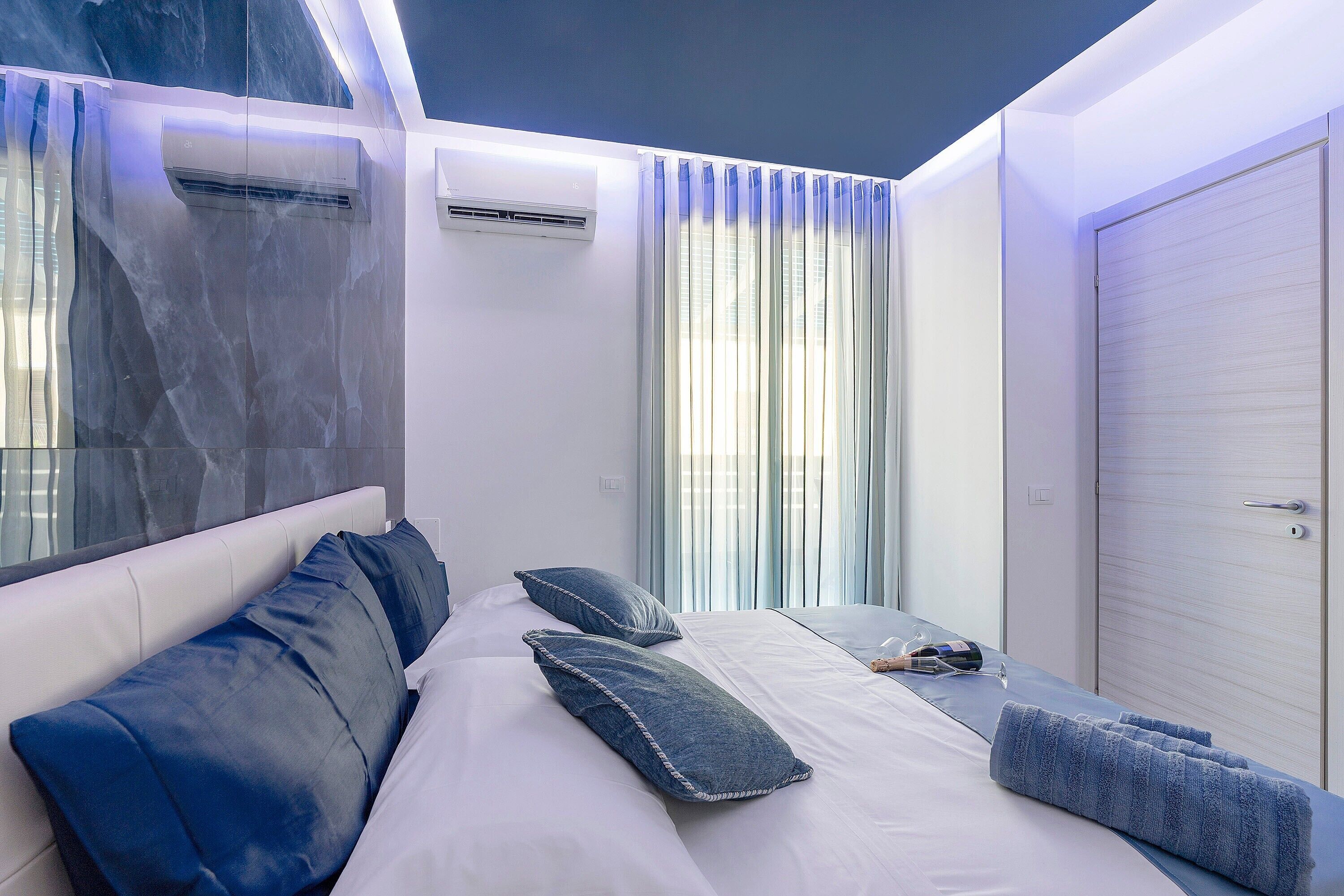 A modern bedroom with a bed, pillows, a bedside table, and an air conditioning unit.