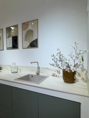 A kitchen with a sink, a vase with flowers, and three framed artworks on the wall.