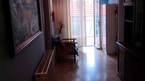 Um corredor com ventilador de teto, um quadro, um sofá, uma mesa com um vaso e uma porta que dá para uma varanda.