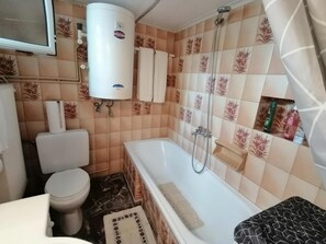 Een badkamer met toilet, bad, douche en boiler.