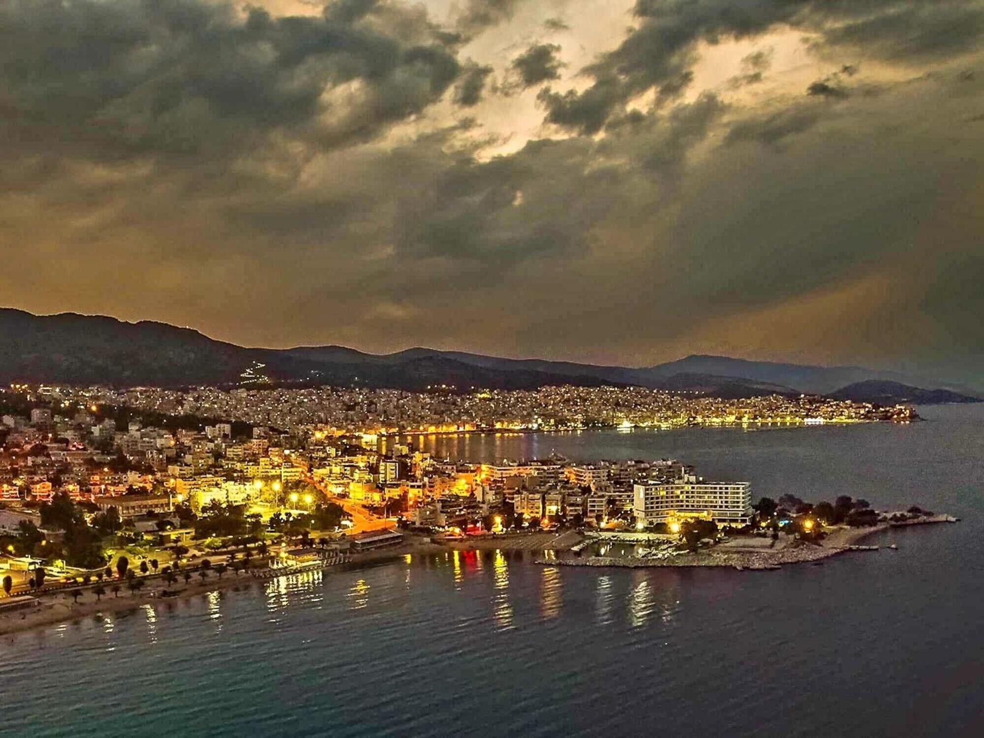 Une vue d’une ville côtière au crépuscule, avec des bâtiments illuminés et un port de plaisance.