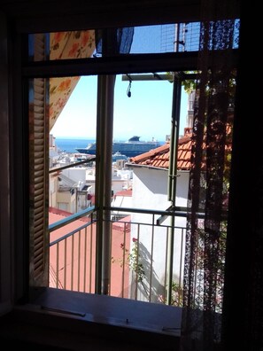 Une fenêtre donnant sur un paysage urbain côtier, avec des bâtiments et un grand navire de croisière.