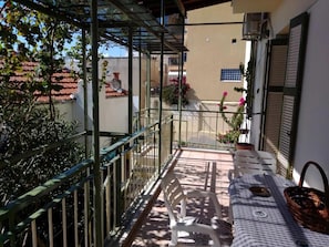 Een balkon met een tafel, stoelen en bloempotten.