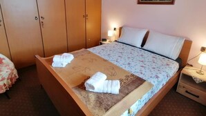 Quarto de hotel com uma cama, um guarda-roupa de madeira, uma mesa de cabeceira com uma luminária e um quadro na parede.