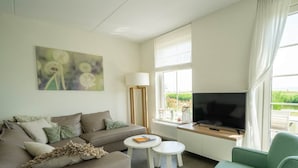 Uma sala de estar com sofá, poltrona verde, mesa de centro, televisão e um quadro na parede.