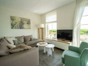 A living room with a sofa, a green armchair, a coffee table, a TV, and a painting on the wall. - Florijn Sauna 6 (Uitdam)