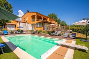 A swimming pool with lounge chairs, a wooden deck, and a house with a tiled roof.