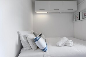 Un lit bien fait, avec des draps blancs, un oreiller à rayures bleues et des serviettes enroulées.