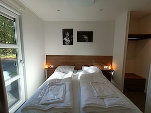 Ein Hotelzimmer mit zwei Betten, einem Holzkopfteil, zwei Nachttischlampen und zwei gerahmten Bildern an der Wand.