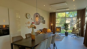 A modern dining area with a table, chairs, a vase with flowers, a clock, and a large window with curtains. - Holiday Home in Otterlo With Terrace (Otterlo)