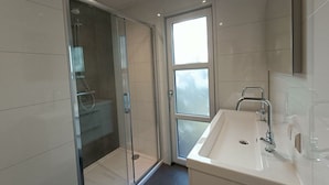 A modern bathroom with a glass-enclosed shower, a sink with a mirror, and a window providing natural light. - Holiday Home in Otterlo With Terrace (Otterlo)