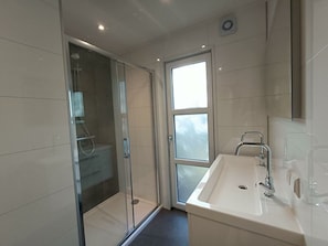 Ein modernes Badezimmer mit einer gläsernen Duschkabine, einem Waschbecken mit Spiegel und einem Fenster für natürliches Licht.