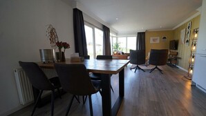 Een moderne eetruimte met een houten tafel, zwarte stoelen en een groot raam met gordijnen.