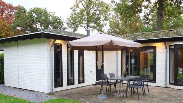 Een terras met een tafel en stoelen, een overdekte parasol en een wit gebouw met zwart omlijste ramen.