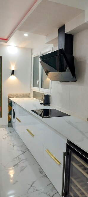 A modern kitchen with a built-in washing machine, a black range hood, and a stainless steel refrigerator.
