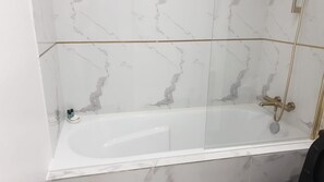 Ein modernes Badezimmer mit einer Glaskabine um eine Badewanne, Marmorwänden und goldenen Armaturen.