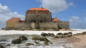 A historic stone building with a red roof, situated by a rocky shoreline.