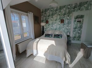 A bedroom with a bed, a window with curtains, a radiator, a wall with a leaf pattern, and a door with a WiFi password sign.