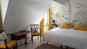 A bedroom with a bed, a chair, a table, and a nightstand.