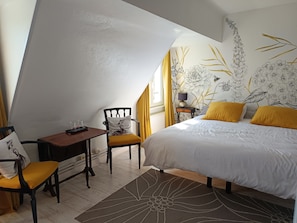 A bedroom with a bed, a chair, a table, and a nightstand.
