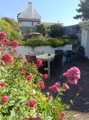 A patio with a table and chairs, surrounded by greenery and flowers.