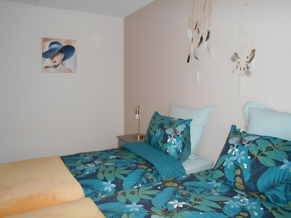 Ein Schlafzimmer mit Bett, Kissen, Nachttisch, Lampe, Wandgemälde und einem Traumfänger.