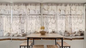 Un espace repas comprenant une table et des bancs, un mur décoré de motifs et une fenêtre.