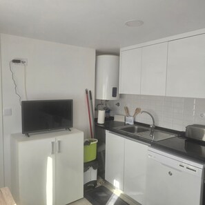 Een compacte keuken met witte kastjes, een inbouw vaatwasser, een spoelbak en een kleine koelkast.