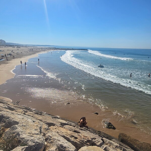 Ein Strand mit Menschen, Wellen und blauem Himmel.
