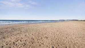 Une vaste plage de sable fin parsemée d’empreintes, un ciel dégagé et une mer calme.