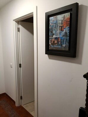 Een gang met een witte deur, een ingelijst schilderij aan de muur en een vloerkleed.