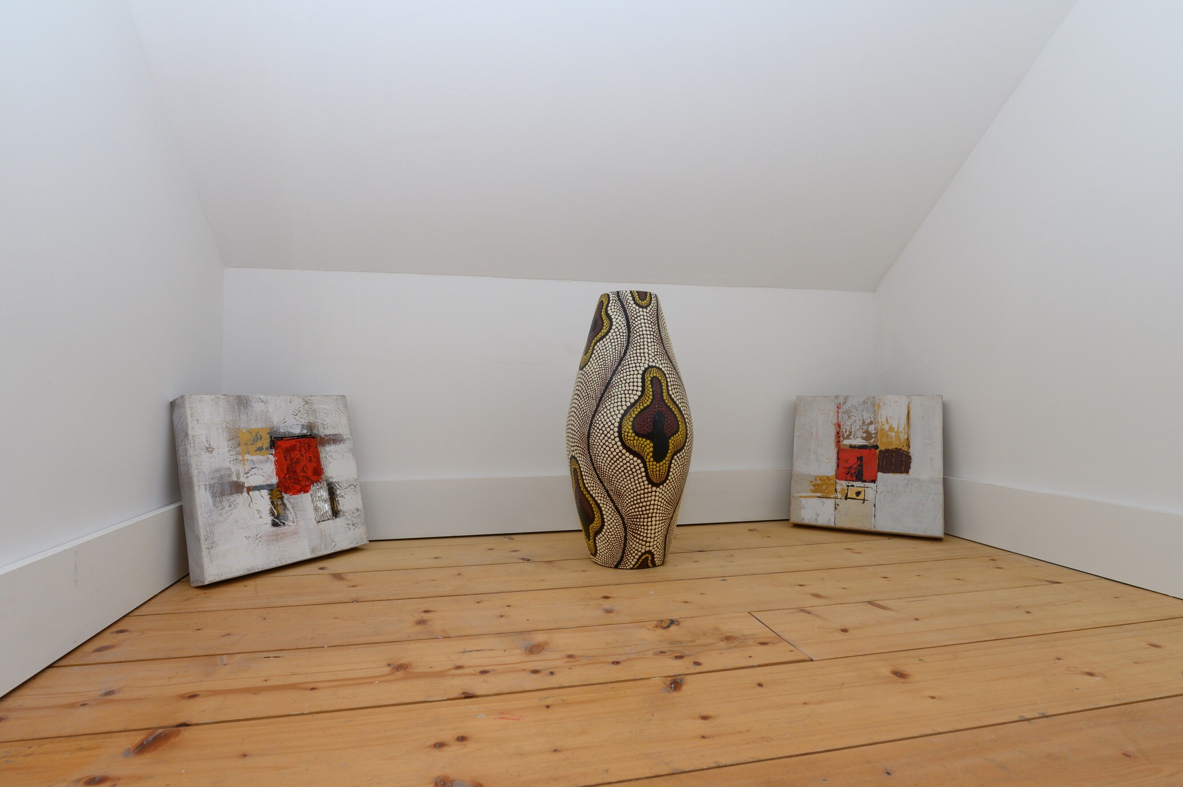 Una habitación con piso de madera, paredes blancas y tres obras de arte en las paredes.