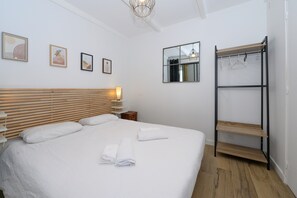 Une chambre d’hôtel bien aménagée, avec un lit, une table de chevet, un miroir, des œuvres d’art accrochées au mur et une armoire intégrée.