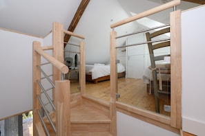 A bedroom with a wooden staircase, a bed, and a large window.