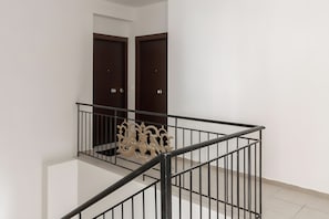 A clean, modern interior with a staircase, two dark wooden doors, and a metal railing.