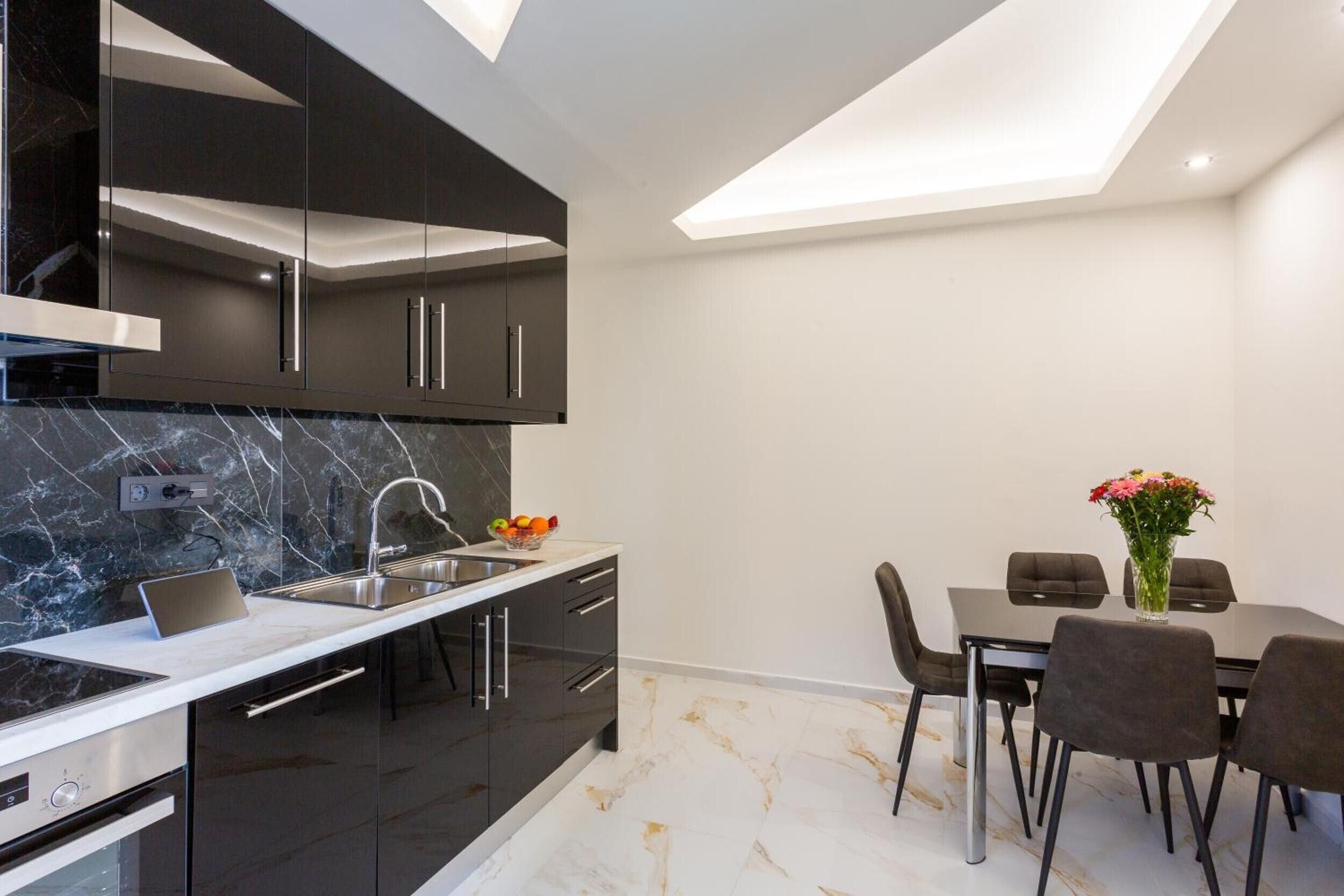 A modern kitchen with dark cabinetry, a marble backsplash, and a dining area with a table and chairs.