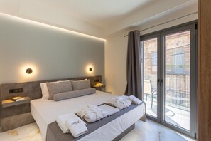 Quarto de hotel moderno com uma cama grande, mesas de cabeceira e uma porta de vidro deslizante para uma área externa.