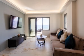 Un salon moderne avec un téléviseur, un canapé, une table basse et une vue sur la mer grâce à de grandes fenêtres.