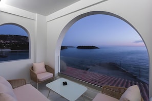 A balcony with a view of the sea, a white table, and wicker chairs.