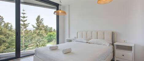 Une chambre moderne avec un grand lit, deux tables de chevet et une vue sur les arbres par une grande fenêtre.