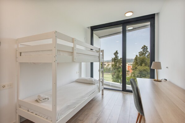 A bunk bed room with a desk and chair, large windows, and a view of the outside.