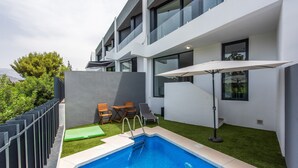 Ein moderner Poolbereich im Freien mit einer fest installierten Poolleiter, einer Liege und einem kleinen Tisch.