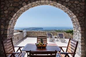 An outdoor seating area with stone walls, a wooden table, and a fruit basket. - Villa 'Cycladic Traditional  Hot Tub' with Wi-Fi and Air Conditioning (Santorini)