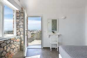 Ein Schlafzimmer mit Steinwand, einem Bett, einer weißen Kommode, einem Spiegel und Blick auf eine Stadt.