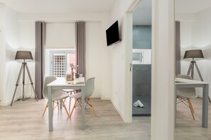 Ein modernes Zimmer mit Esstisch, Stühlen, einem Flachbildfernseher und einer Lampe.