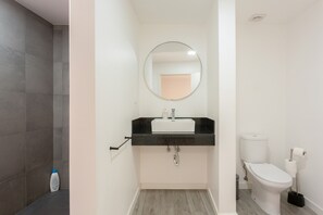 Un baño con un lavabo blanco, encimera negra y un espejo redondo.