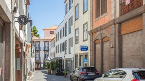 Una estrecha calle empedrada bordeada de edificios de varios pisos, algunos con letreros visibles.