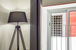 Een driepootvloerlamp, een raam met metalen tralies, en een deur met een rode accentkleur.