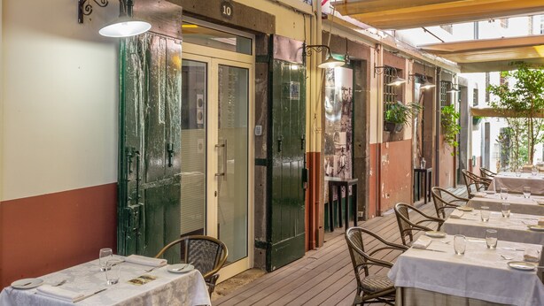 Un área de comedor al aire libre con mesas y sillas, una terraza de madera y una puerta verde.